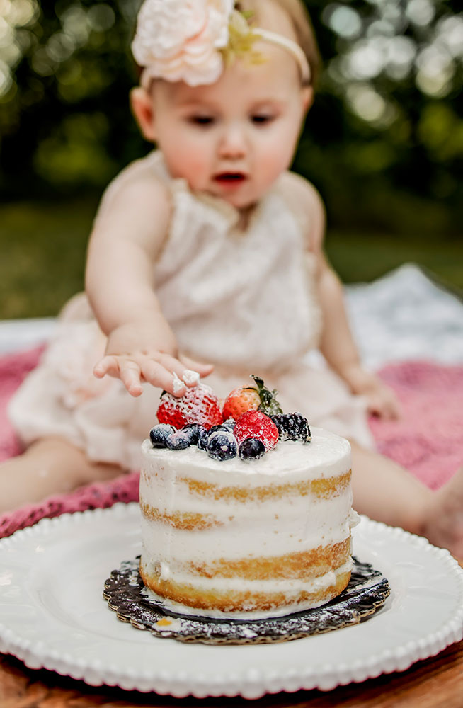 At a first birthday photo session a baby girl eats a strawberry off of her cake and a cake smash picture session