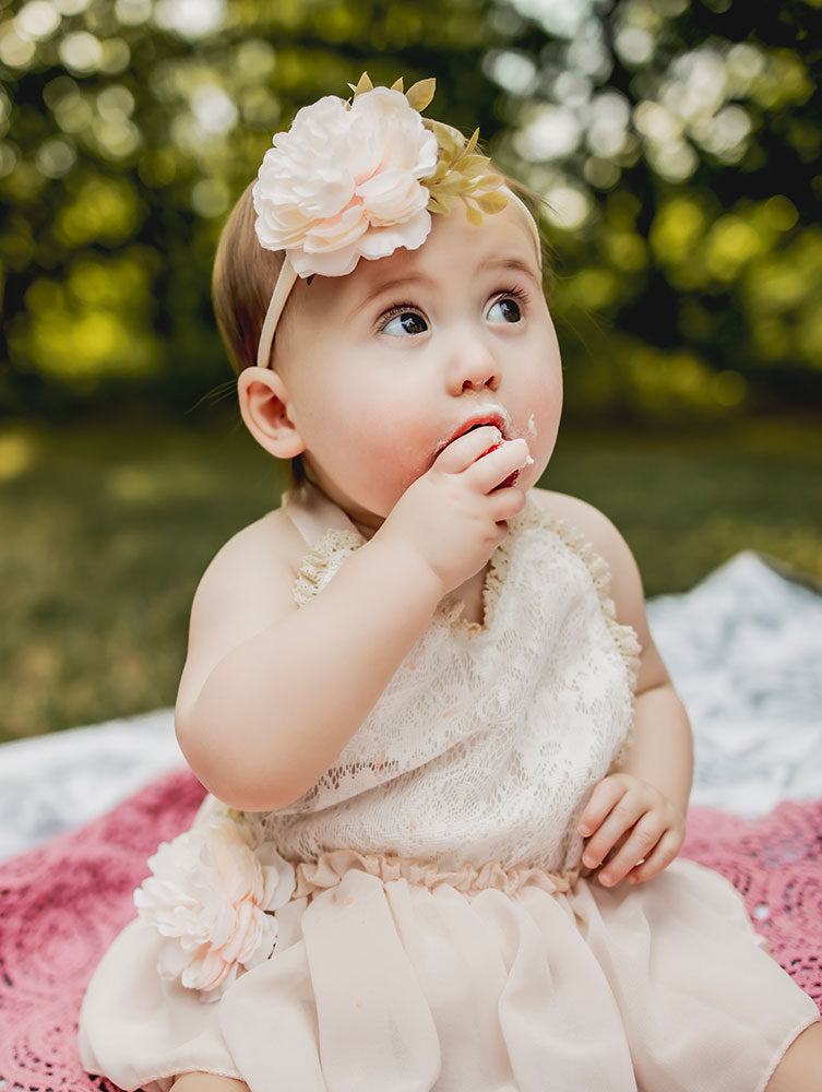 At a first birthday photo session a baby girl eats a strawberry off of her cake and a cake smash picture session