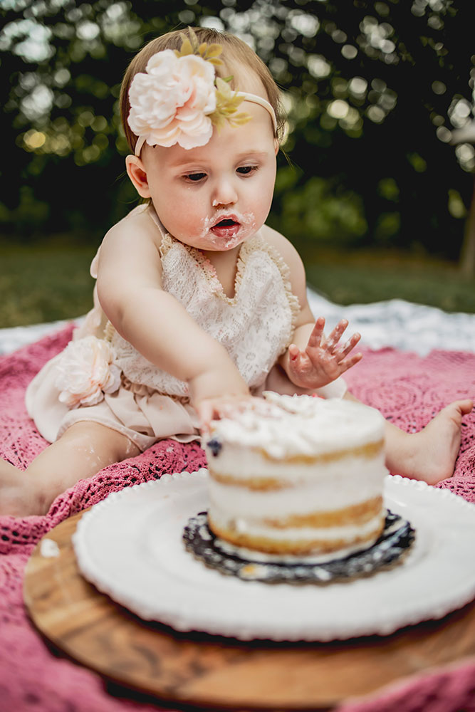 At a first birthday photo session a baby girl puts her hand in the cake and a cake smash picture session