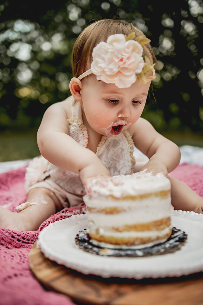 At a first birthday photo session a baby girl eats her cake at a cake smash picture session