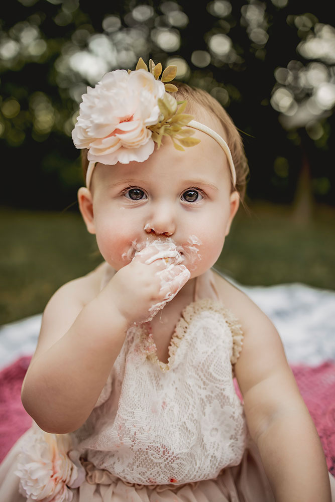 At a first birthday photo session a baby girl eats a icing off of her cake and a cake smash picture session