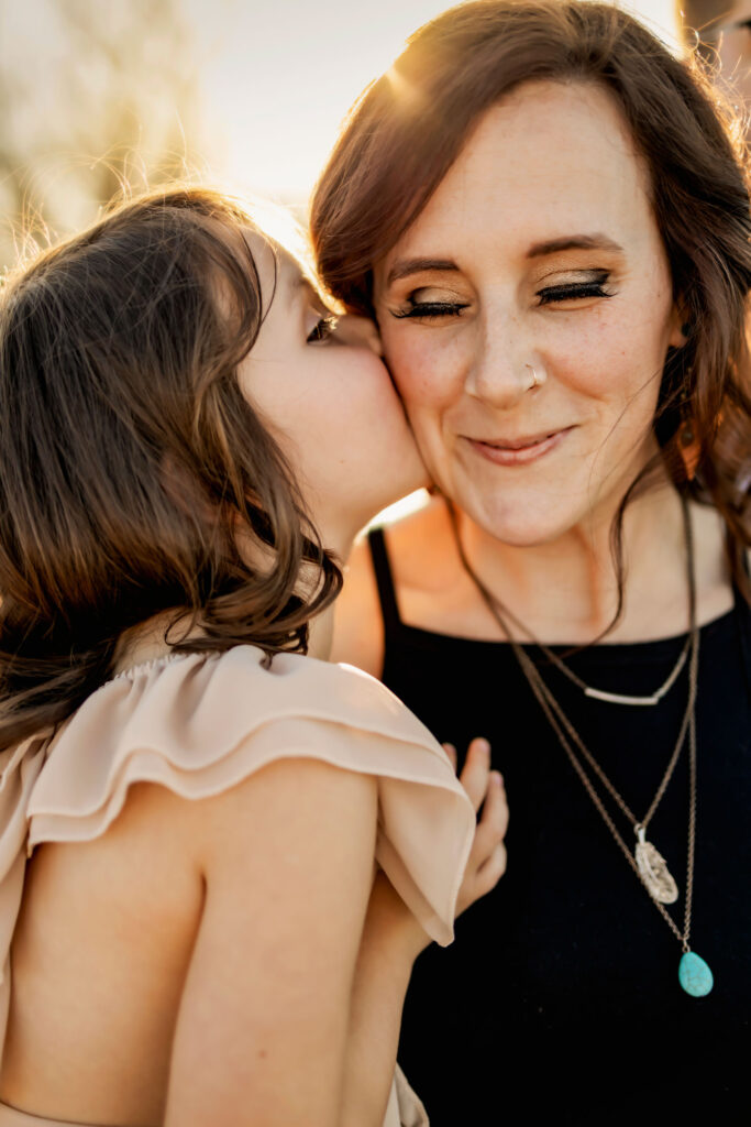 A little girl gives her mom a kiss in the sunshine at a photo session at Lake Grapevine with Anna Roorda Photography.