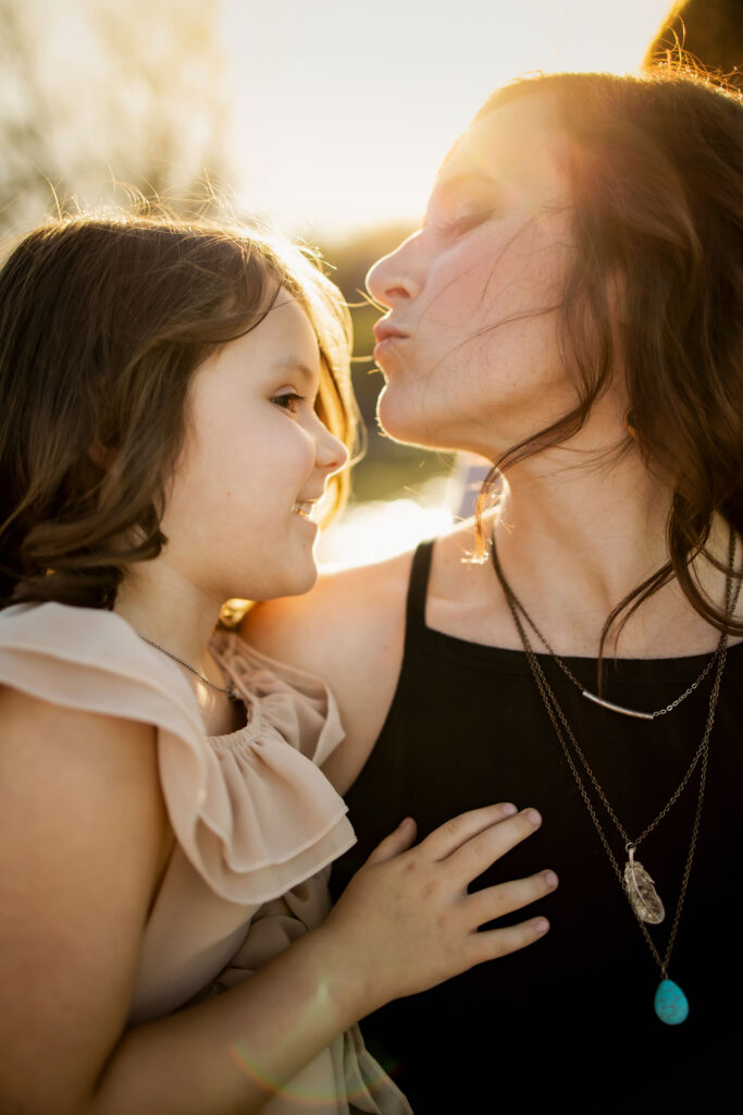 A mom gives her daughter a kiss in the sunshine at a photo session at Lake Grapevine with Anna Roorda Photography.