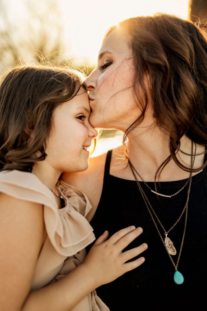 A mom gives her daughter a kiss in the sunshine at a photo session at Lake Grapevine with Anna Roorda Photography.