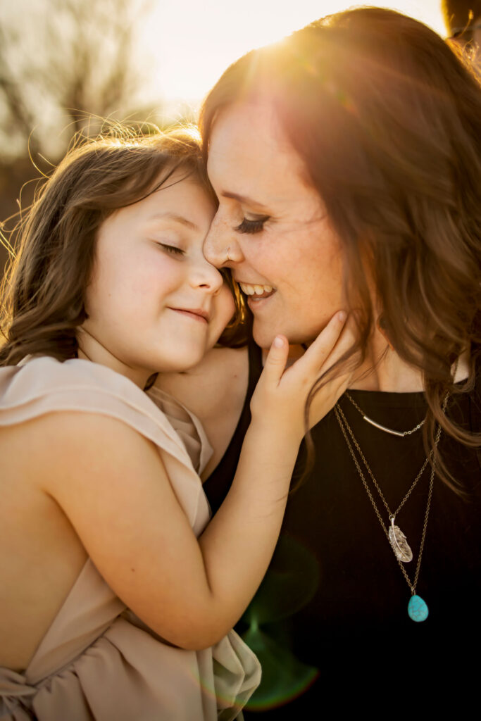 A mom gives her daughter a kiss in the sunshine at a photo session at Lake Grapevine with Anna Roorda Photography.