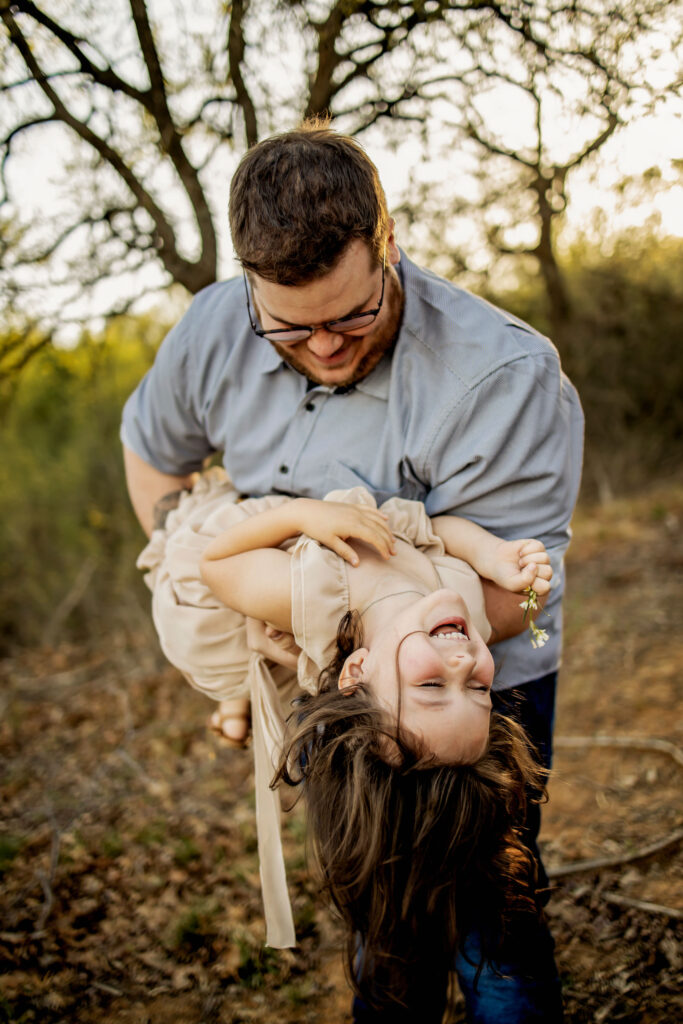 A dad plays with his daughter in the sunshine at a spring photo session at Lake Grapevine with Anna Roorda Photography.