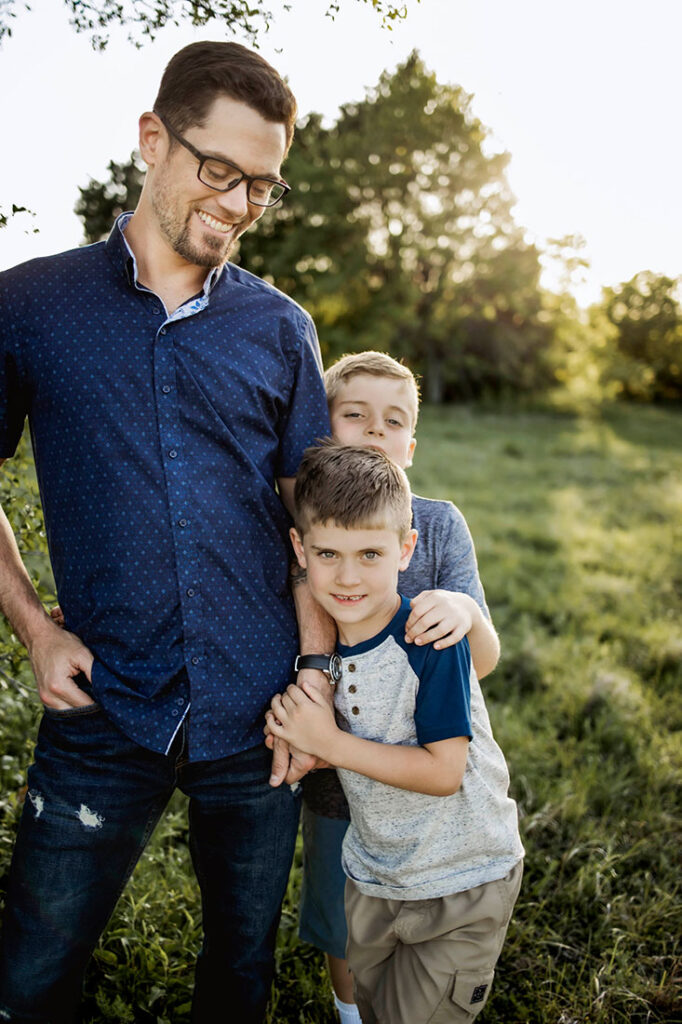 Two boys lean into dad and play while at a session with Anna Roorda Photography in Plano, TX at arbor hills nature preserve.