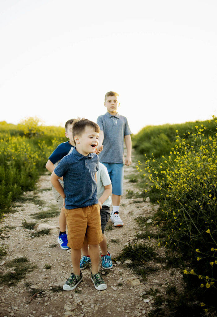 A family of four boys at a Spring half session walks down a path at Arbor Hills in Plano, TX with yellow wild flowers.