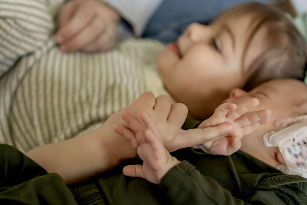 a toddler holds her finger out for her newborn brother to grasp at an in home session